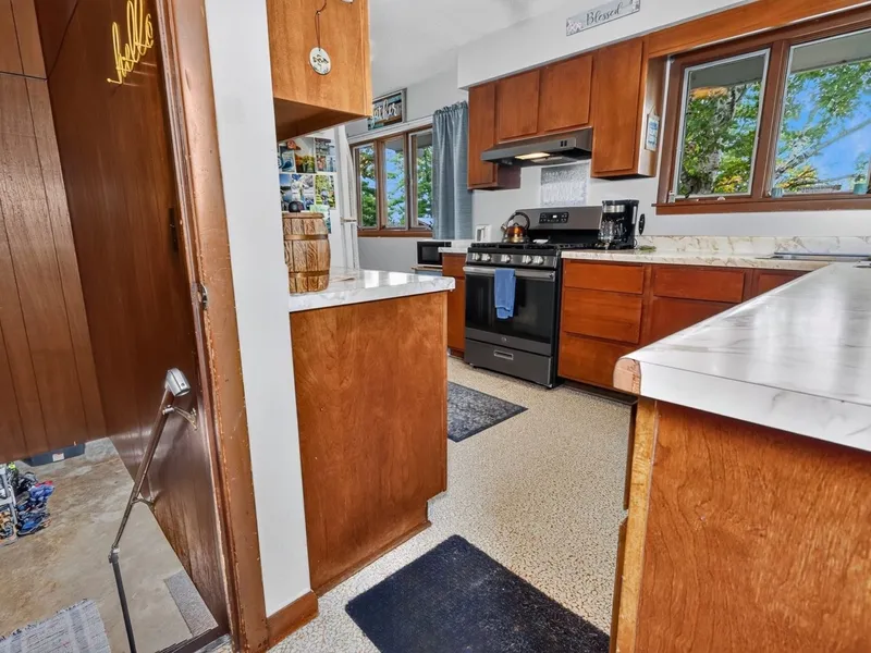 Living room with wood paneling, a wood stove, and windows toward the kitchen